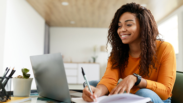 Woman using a laptop and writing in a notebook