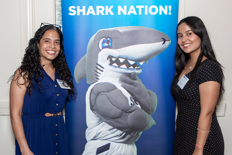 NSU alumni pose next to a shark nation banner.