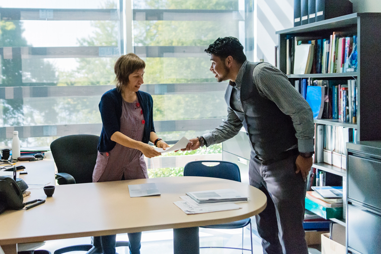 Student giving papers to admissions school counselor at the office