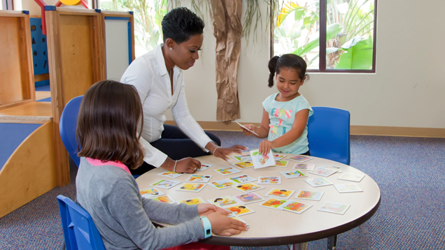 Teacher sitting in desk doing learning activity with kids