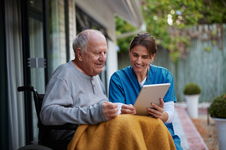 Friendly nurse and senior man on wheelchair using digital tablet