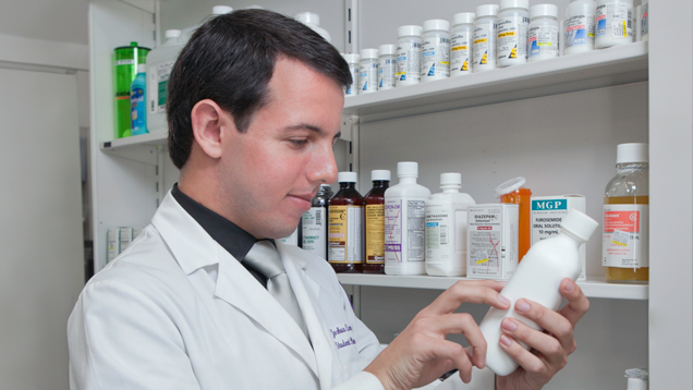 Young male pharmacist reading bottle label next to shelfs