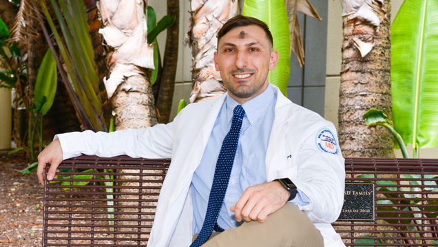 NSU medical student wearing white coat sitting on a bench.