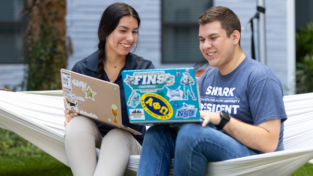 Two students using laptops in campus outdoors