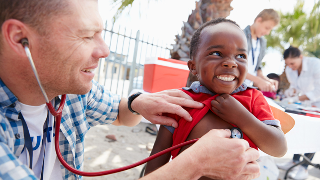 Volunteer doctor using stethoscope on young child.