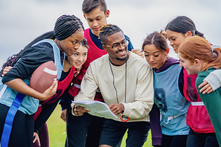 Group of students huddle together with their coach during a game of flag football