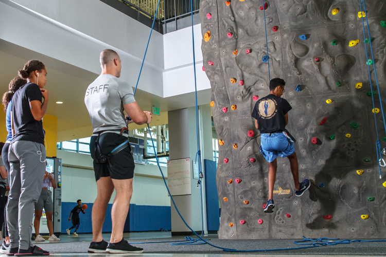 Staff climbing wall attendant helping student