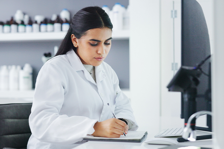 Scientist using a computer and writing in her notebook