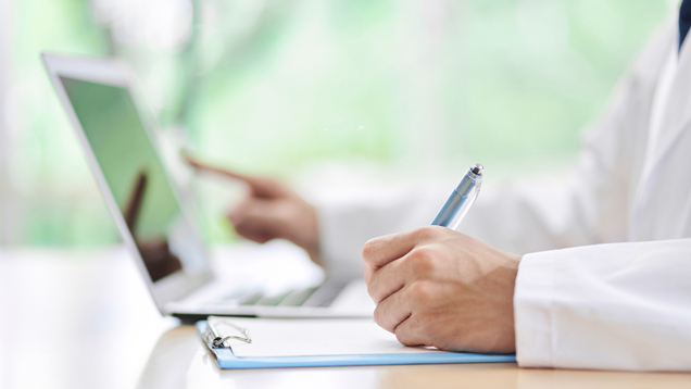 Medical professional writing and pointing to laptop screen