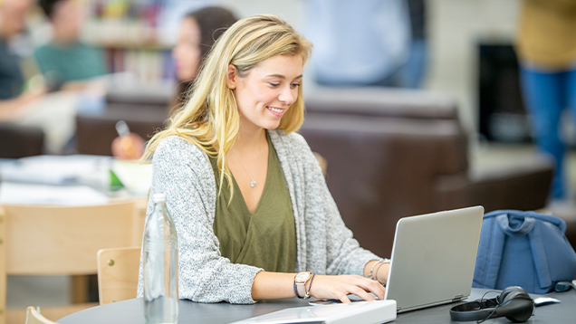 Student smiling and using a laptop to research