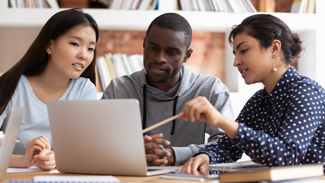 Students sit at a desk with a laptop working together on a project