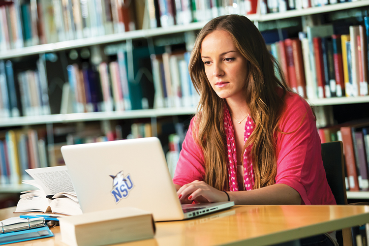 NSU student using a laptop in the library