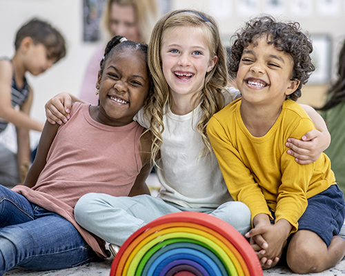 Three young children posing and smiling for a photo in a classroom